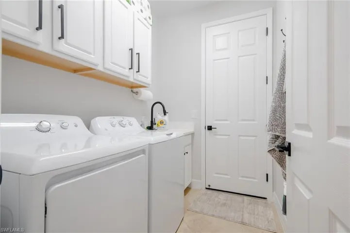 Laundry room featuring washer and clothes dryer, light tile patterned flooring, cabinets, and sink