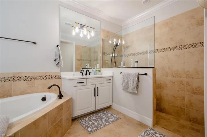 Bathroom featuring tile patterned floors, crown molding, vanity, and shower with separate bathtub