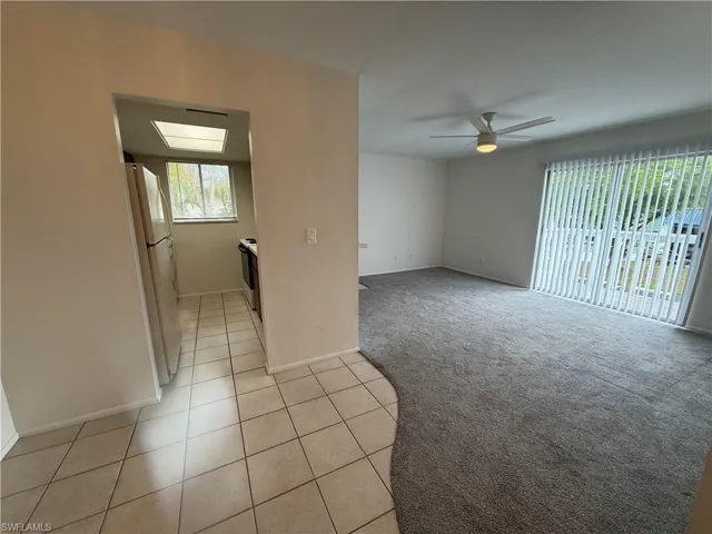 Unfurnished room featuring a ceiling fan, light tile patterned floors, baseboards, and light carpet