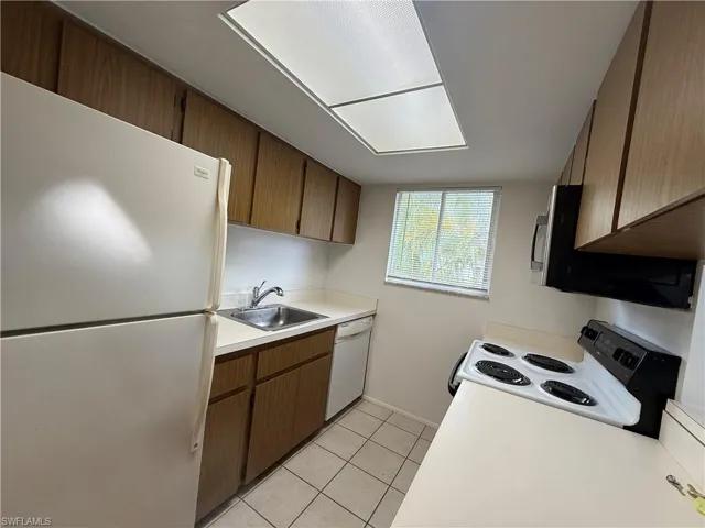 Kitchen with white appliances, a sink, light countertops, and light tile patterned floors