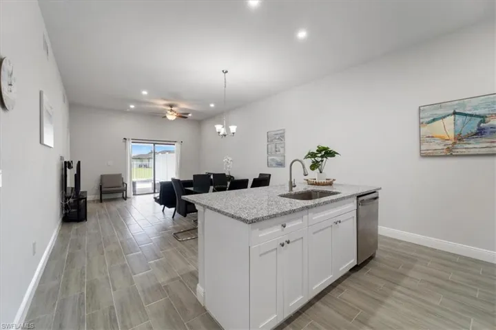 Kitchen with light stone counters, wood tiled floors, white cabinets, and an island with sink