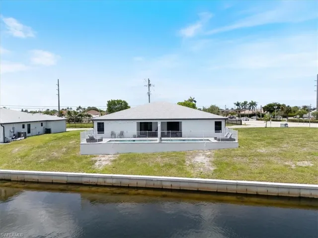 Back of house featuring an outdoor pool, a lawn, a water view, and a patio area