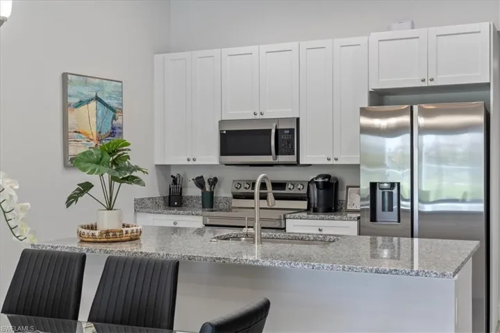 Kitchen with light stone countertops, stainless steel appliances, white cabinetry, and a kitchen breakfast bar