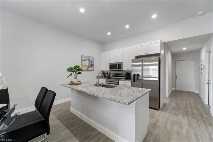 Kitchen featuring stainless steel appliances, wood tiled floors, light stone countertops, white cabinets, and a center island with sink