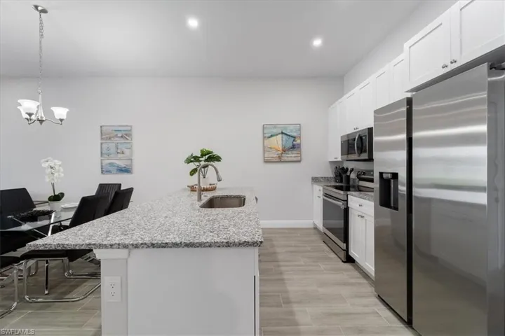 Kitchen featuring stainless steel appliances, white cabinetry, light stone counters, and a kitchen island with sink