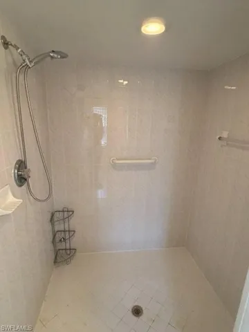 Tiled shower stall featuring a handheld showerhead, recessed lighting, and a grab bar