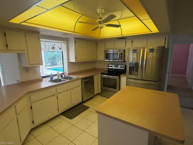 Kitchen featuring a ceiling fan, white cabinetry, light-toned countertops, a stainless steel appliance suite, and a central island