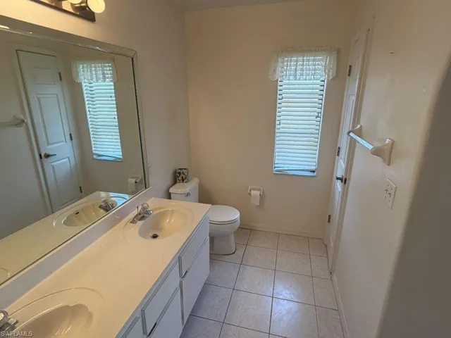 Bathroom featuring a dual vanity with integrated sinks, a wide mirror, and tile flooring