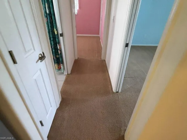 Carpeted hallway featuring white paneled doors and varied wall colors in visible rooms