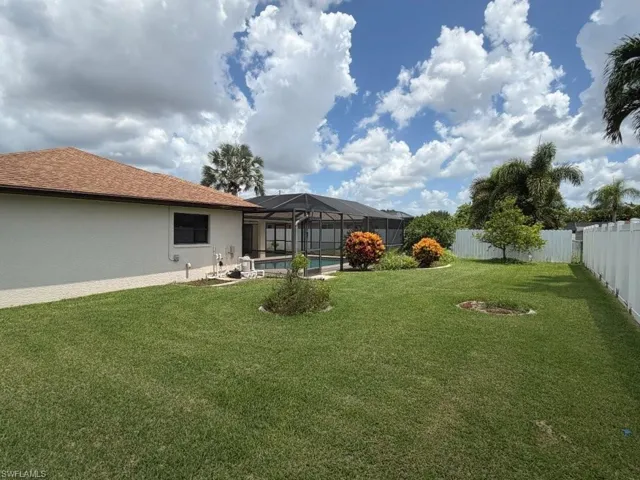 Expansive backyard featuring a screened-in pool enclosure, mature tropical landscaping, and a privacy fence