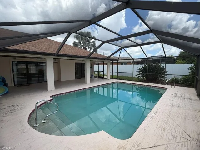 Screen-enclosed swimming pool featuring a curved entry, light-colored deck, and direct access to interior spaces through sliding glass doors