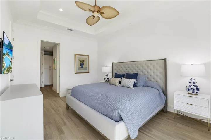 Bedroom with ornamental molding, light wood-type flooring, ceiling fan, and a tray ceiling