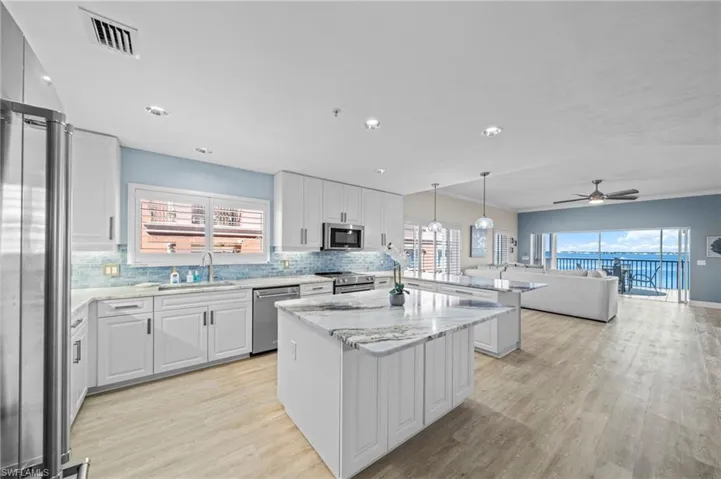 Kitchen featuring open floor plan, white cabinetry, tasteful backsplash, light stone counters, and a kitchen island