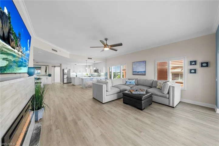 Living room with crown molding, light wood finished floors, ceiling fan, healthy amount of natural light, and a fireplace
