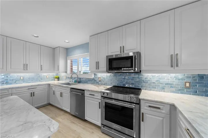 Kitchen featuring appliances with stainless steel finishes, white cabinetry, light wood-style floors, decorative backsplash, and light stone counters