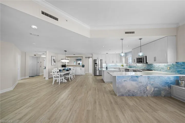 Kitchen featuring white cabinetry, tasteful backsplash, pendant lighting, a peninsula, and crown molding