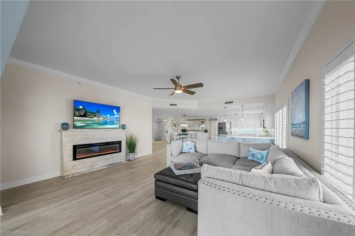 Living room with light wood-type flooring, crown molding, a ceiling fan, and a glass covered fireplace