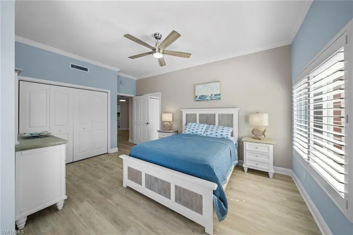 Bedroom with crown molding, light wood-style flooring, a ceiling fan, and a closet