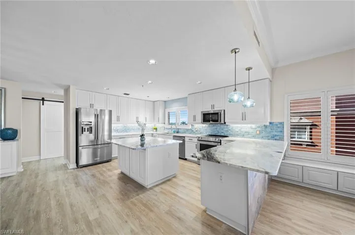 Kitchen with a barn door, decorative backsplash, white cabinetry, decorative light fixtures, and stainless steel appliances