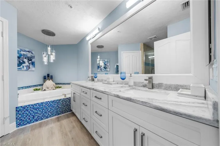 Full bath featuring light wood finished floors, double vanity, a stall shower, a bath, and a textured ceiling