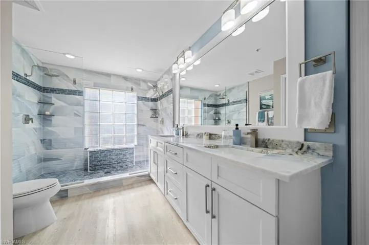 Full bath featuring light wood finished floors, double vanity, a stall shower, a bath, and a textured ceiling