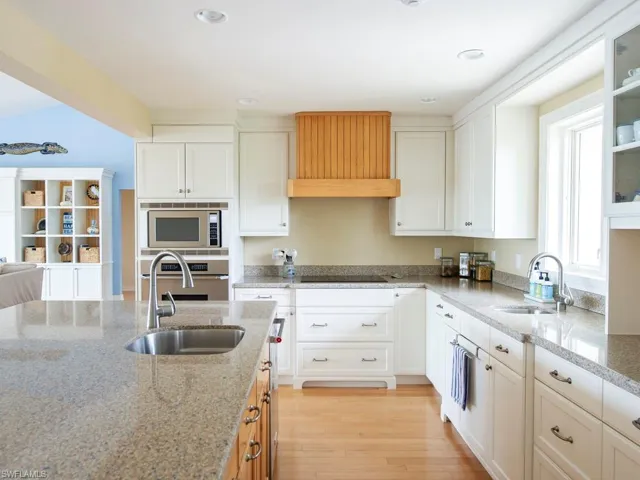 Kitchen with white cabinetry, light stone counters, light wood finished floors, stainless steel appliances, and glass insert cabinets