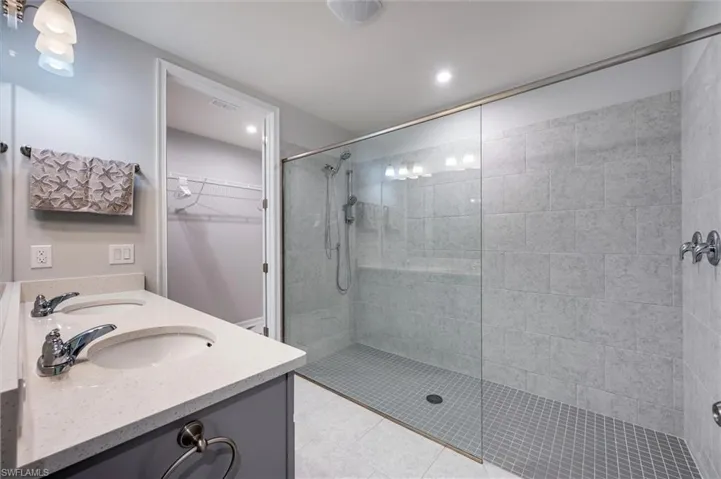 Primary bath featuring a spacious closet, a walk in shower, double vanity, and light tile patterned floors