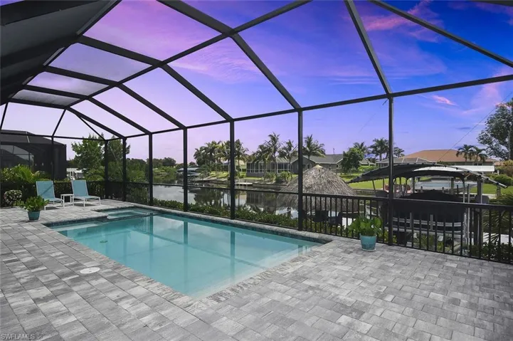 Pool at dusk featuring a water view, a patio, a gazebo, and a pool with connected hot tub