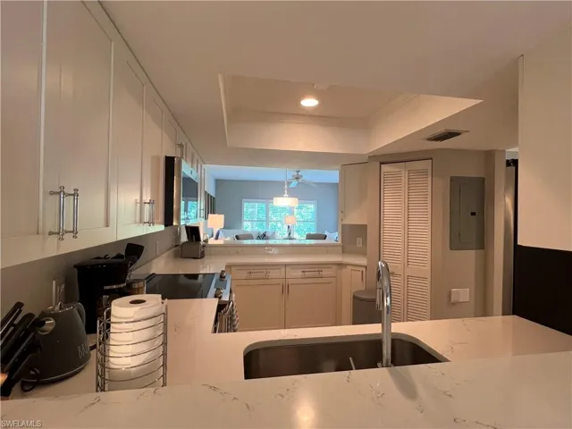 Kitchen featuring white cabinetry, electric panel, light stone countertops, and a tray ceiling