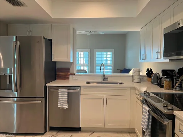 Kitchen featuring light tile patterned flooring, sink, stainless steel appliances, and white cabinets