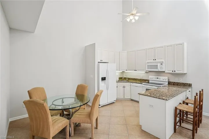Kitchen featuring dark stone countertops, white appliances, a peninsula, white cabinets, and a towering ceiling
