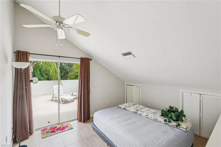 Tiled bedroom featuring vaulted ceiling, access to outside, multiple closets, and ceiling fan