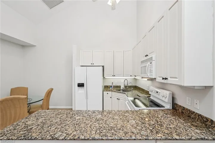 Kitchen featuring white appliances, dark stone counters, white cabinetry, a peninsula, and high vaulted ceiling