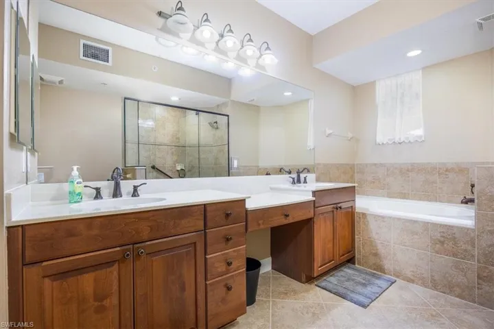Bathroom featuring a stall shower, double vanity, a bath, and light tile patterned floors