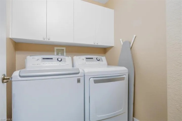 Washroom featuring independent washer and dryer, a textured wall, and cabinet space