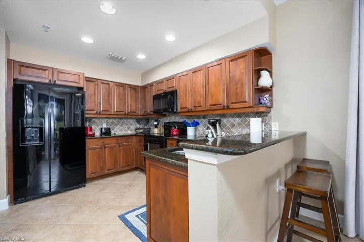 Kitchen with brown cabinets, black appliances, a peninsula, a kitchen bar, and dark stone countertops