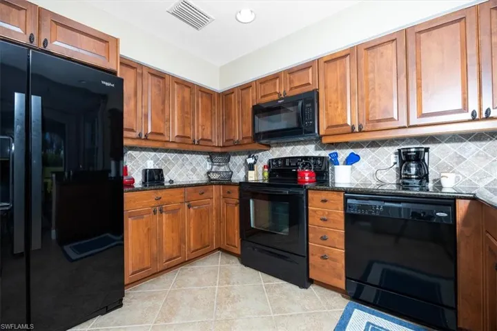 Kitchen with black appliances, brown cabinets, dark stone countertops, and light tile patterned floors