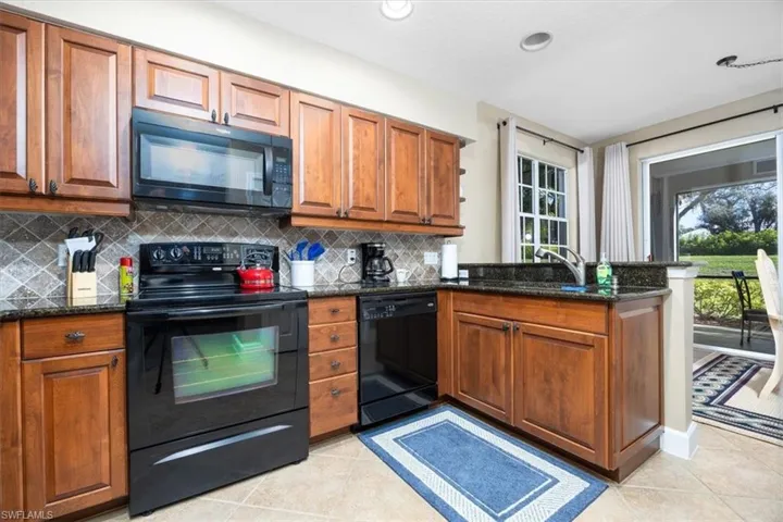 Kitchen featuring black appliances, brown cabinetry, a peninsula, dark stone countertops, and light tile patterned floors