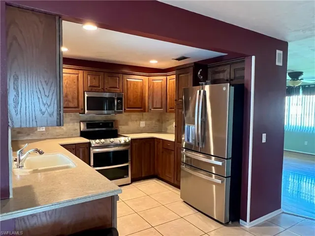 Kitchen with appliances with stainless steel finishes, light tile patterned floors, backsplash, light stone countertops, and recessed lighting