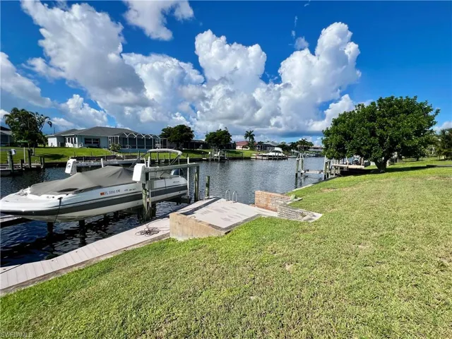 Dock area featuring boat lift, a lawn, a water view, and a residential view
