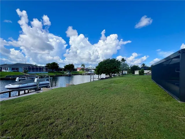 View of grassy yard featuring a water view, a boat dock, and a lanai