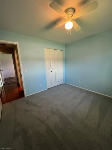 Unfurnished bedroom with ceiling fan, dark carpet, and a closet