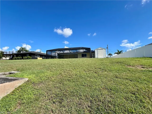 View of green lawn featuring glass enclosure, a storage unit, and a sunroom