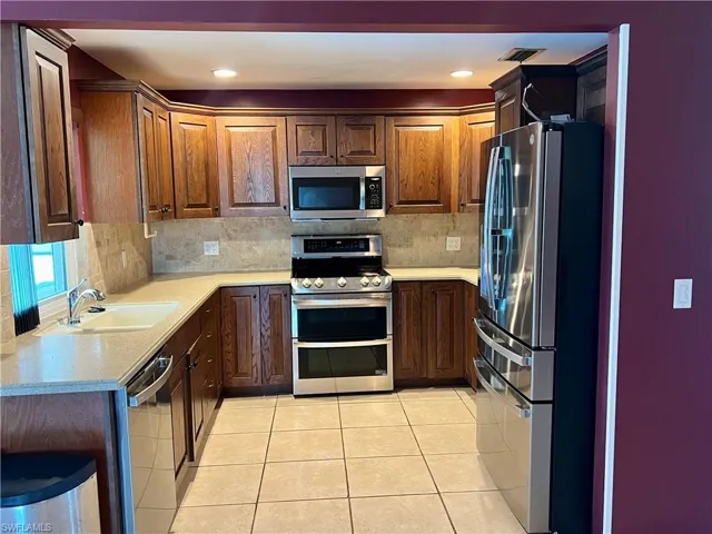 Kitchen with appliances with stainless steel finishes, decorative backsplash, light tile patterned floors, light stone countertops, and recessed lighting