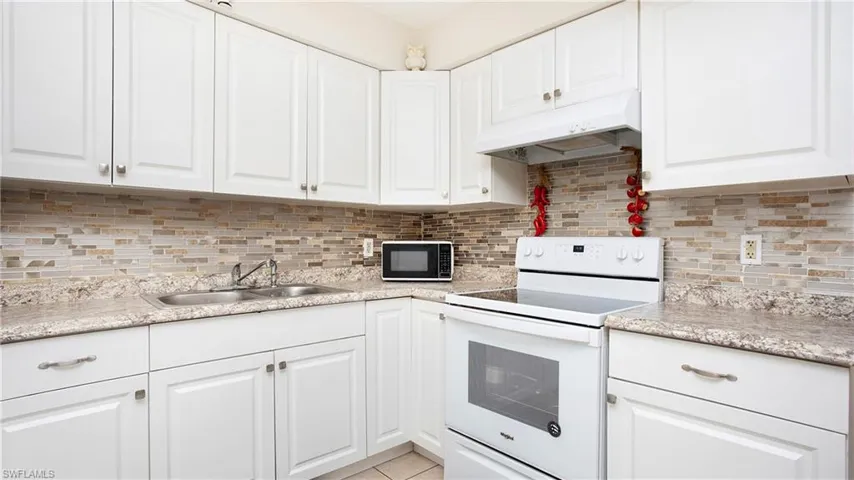 Kitchen with white electric range, black microwave, under cabinet range hood, a sink, and white cabinetry