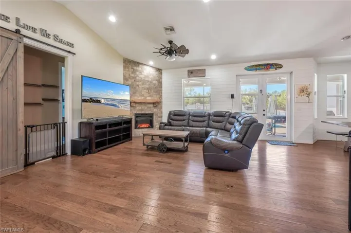 Living area featuring hardwood / wood-style flooring, a ceiling fan, a barn door, a stone fireplace, and visible vents