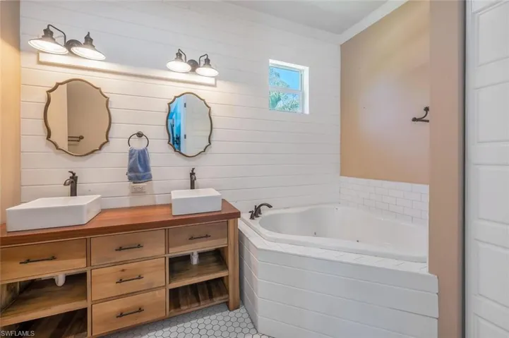 Full bath featuring a jetted tub, double vanity, ornamental molding, and a sink