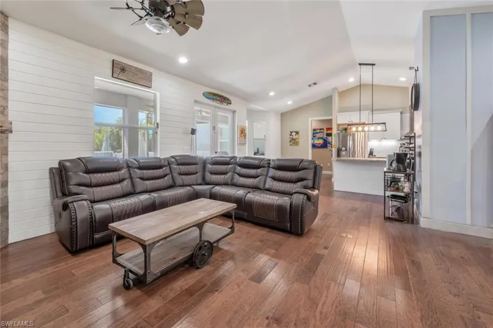 Living room featuring dark wood-type flooring, lofted ceiling, recessed lighting, and ceiling fan with notable chandelier