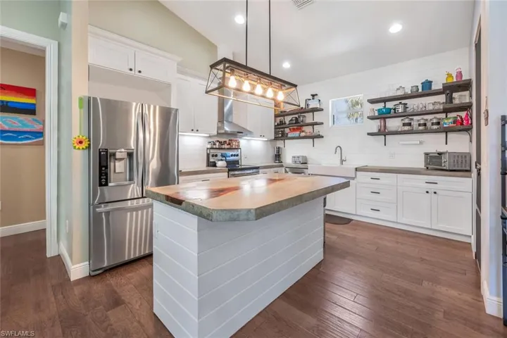 Kitchen with open shelves, wall chimney exhaust hood, dark wood finished floors, a center island, and stainless steel appliances