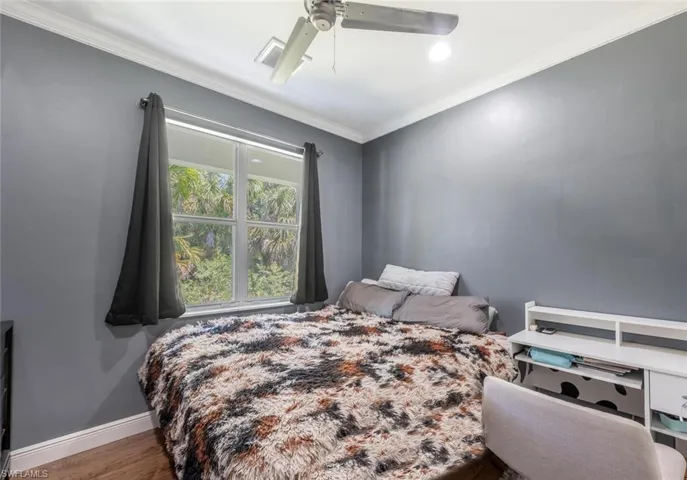 Bedroom with baseboards, wood finished floors, ornamental molding, and a ceiling fan